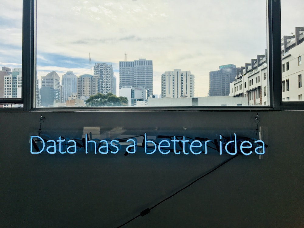 Blue neon sign that reads 'Data has a better idea' with a city skyline in the background