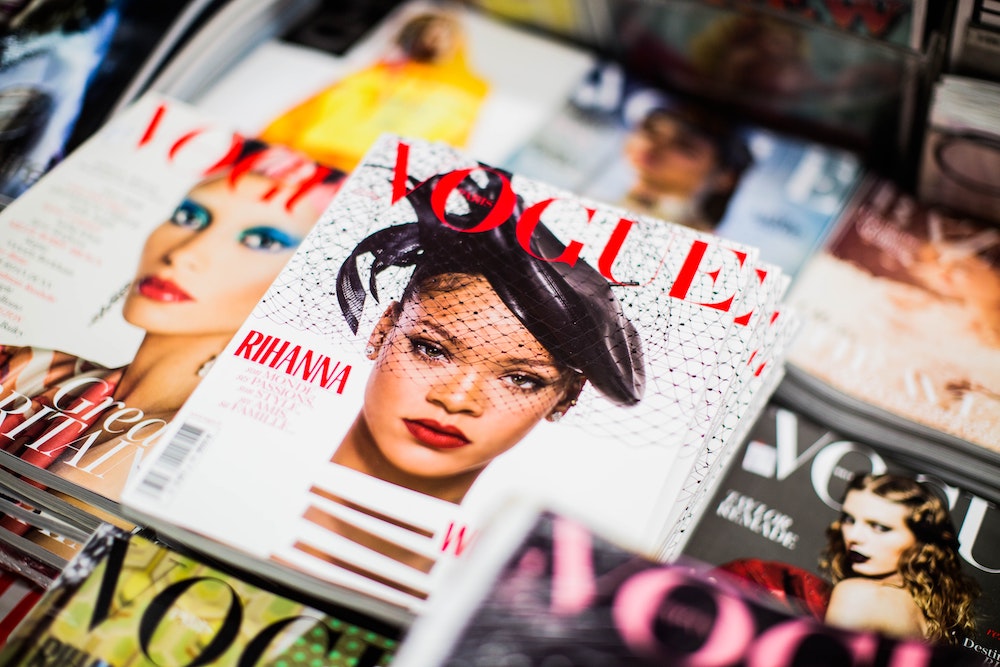 A table covered in different issues of Vogue magazine, with Rihanna in focus on one cover.