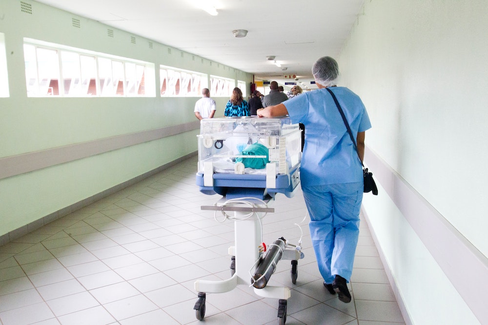 A nurse wheeling a new-born baby through a hospital corridor.