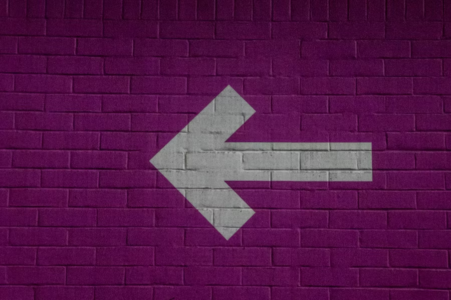 A large white arrow painted on a purple brick wall pointing to the left.