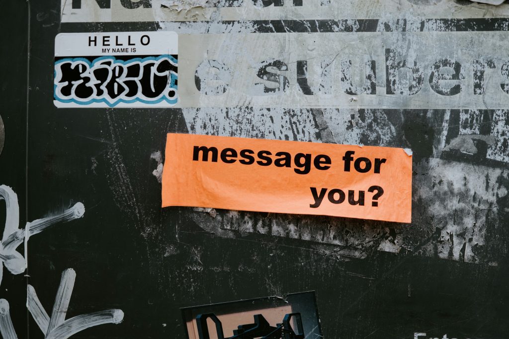 An orange sticker reading “message for you?” attached to a worn, graffiti-covered surface.