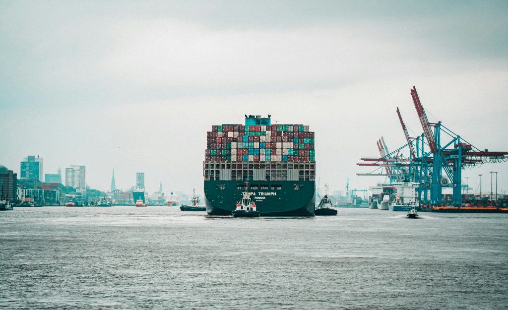A large container ship entering a busy port, reflecting global supply chain movement and logistics operations.