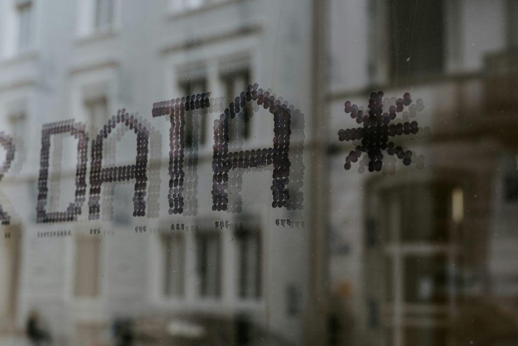 The word “DATA” and an asterisk symbol made from small circular stickers on a glass window, with blurred buildings visible in the background.