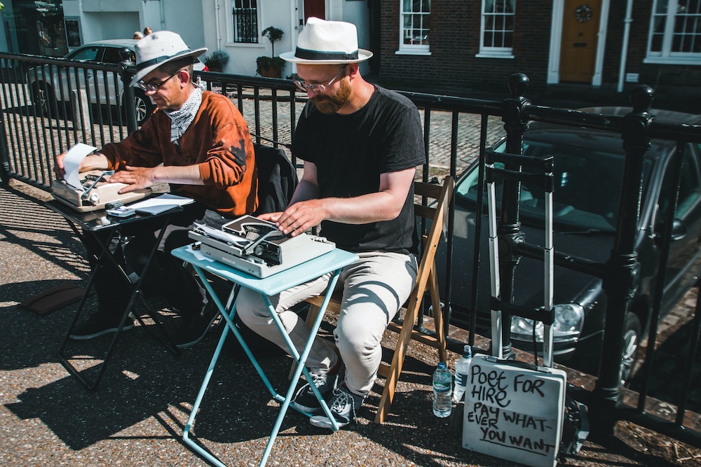 Two men sitting outside using typewriters