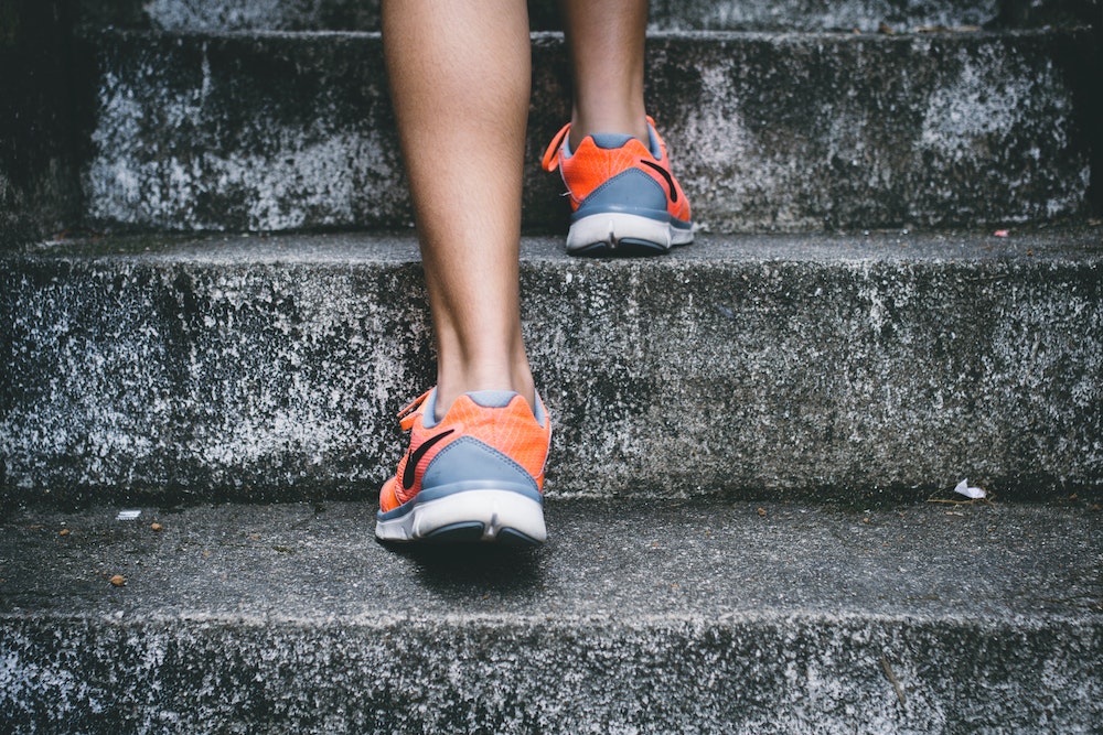 A person wearing grey and orange sneakers climbing up cement steps.