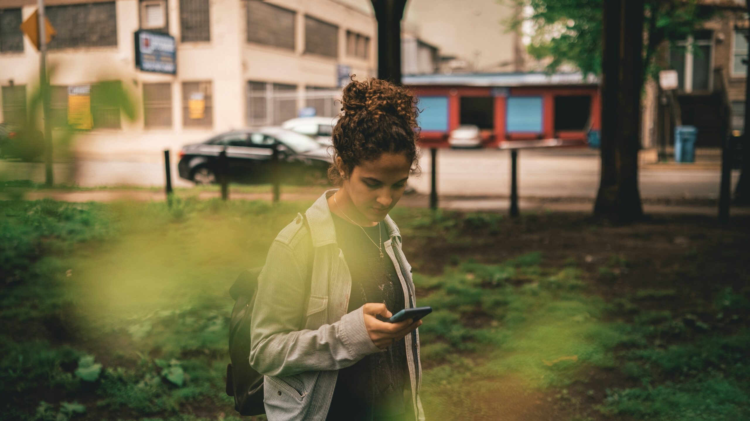 a gen z woman standing in the grass looking at her cell phone