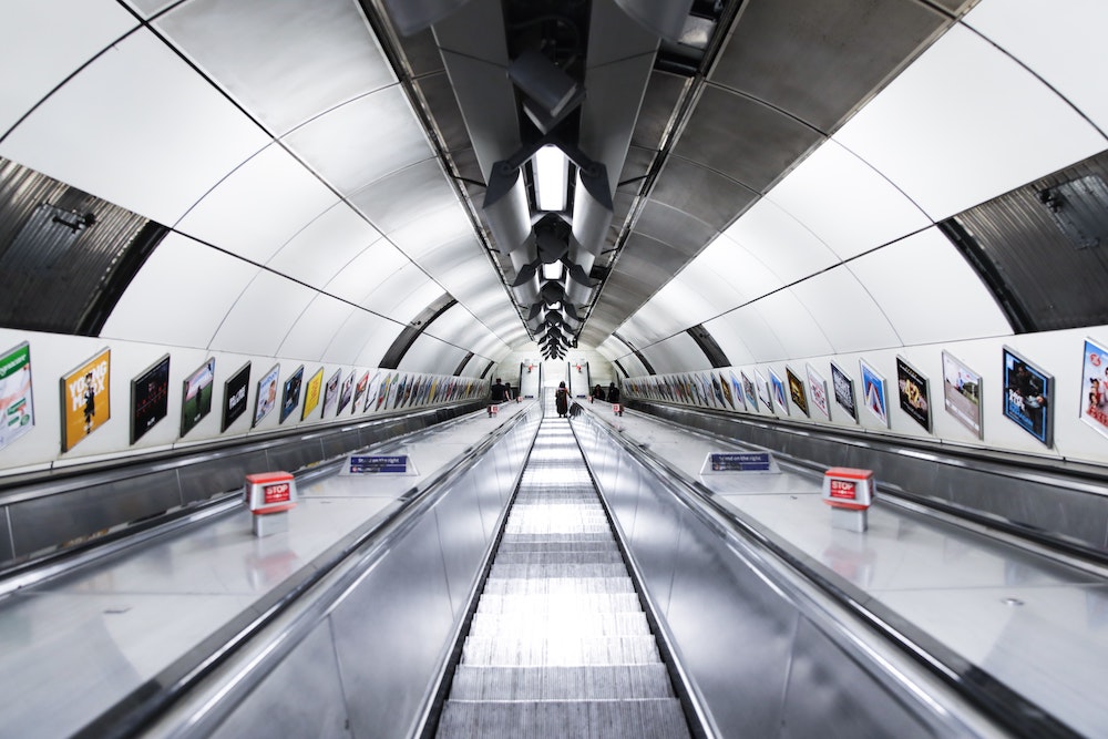 An escalator in an underground subway station, lined with posters from well-known brands.