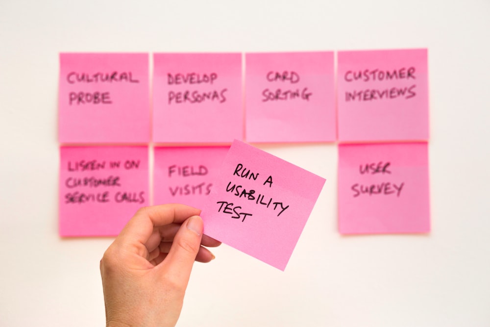 person holding pink sticky note reading "run a usability test"