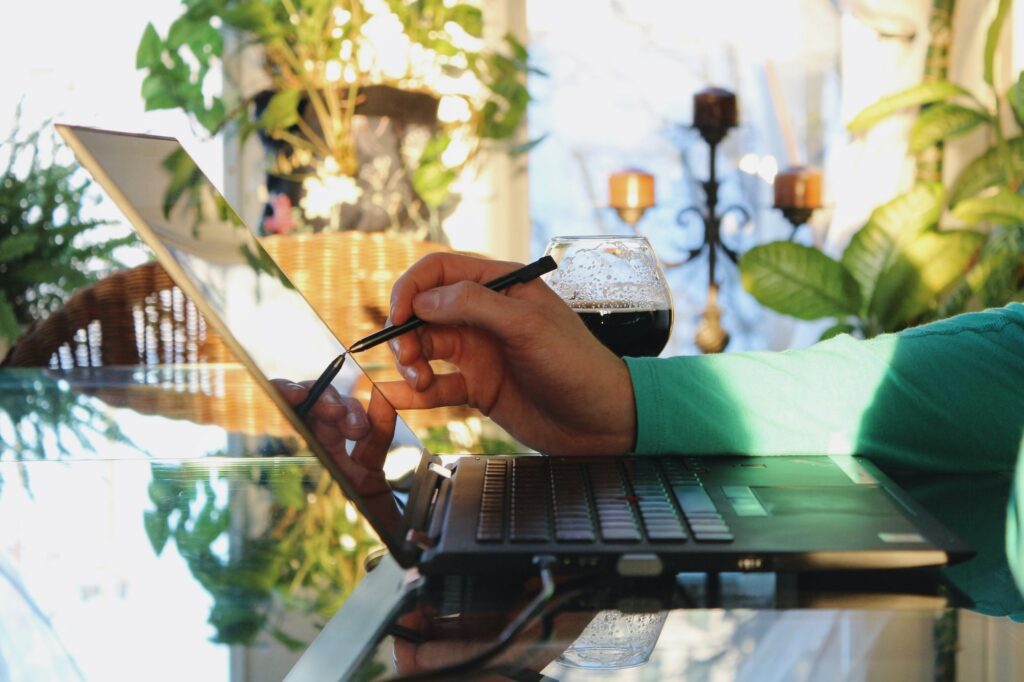 Person using a stylus on a laptop with a drink beside them.