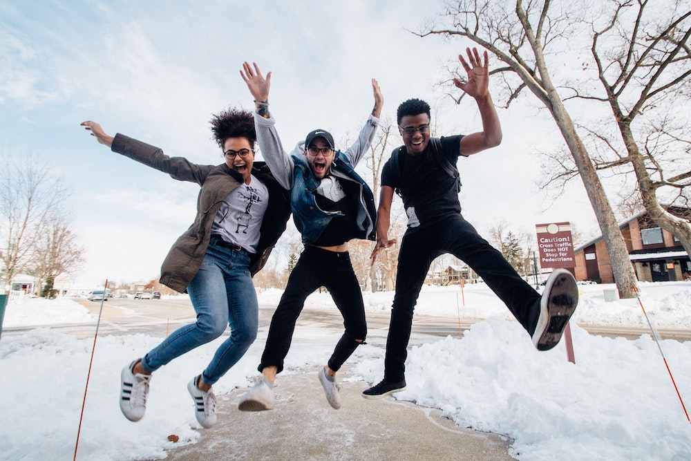 Three people jumping up together on a snowy street