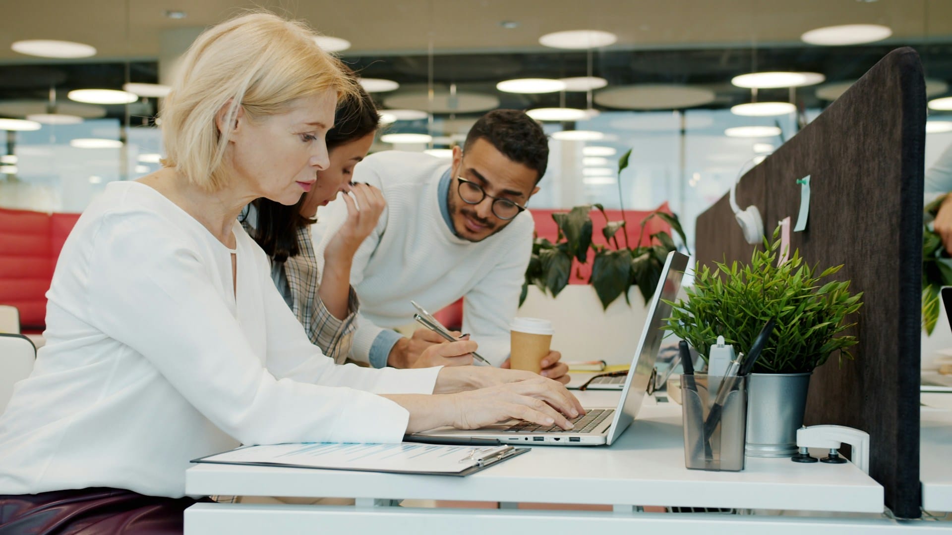Three researchers collaborating on a survey draft at a laptop in a modern office.
